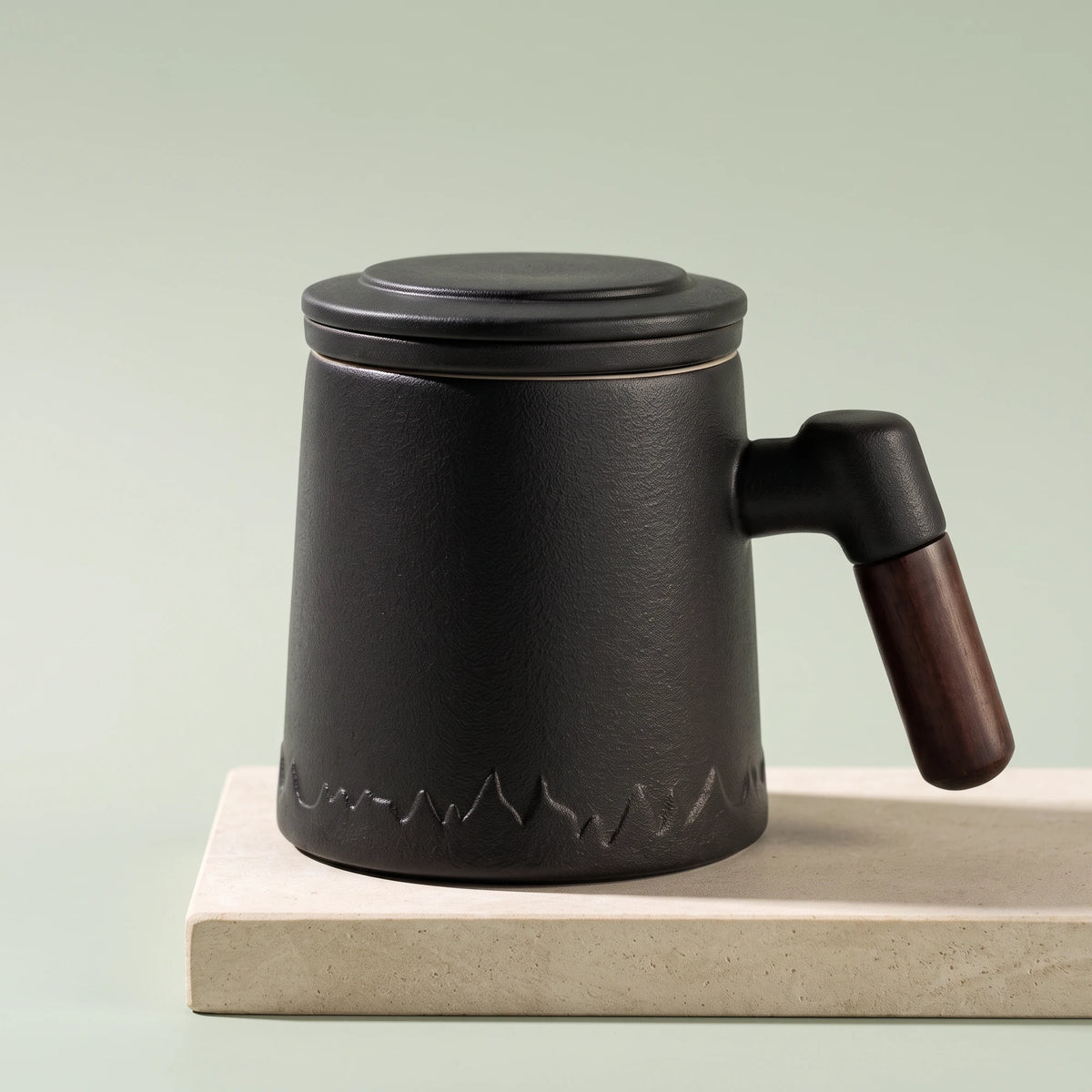 Everest ceramic tea infuser mug, Noir Black, on a stone tile