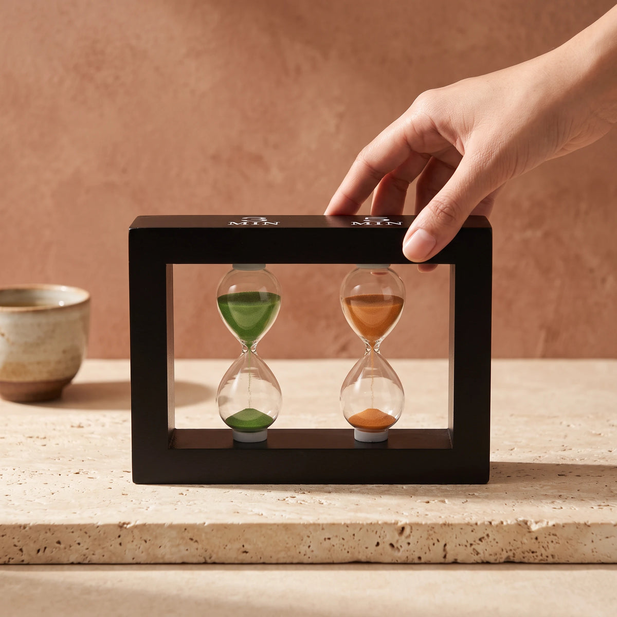 Hand turning the Happy Hour tea timer on a stone shelf