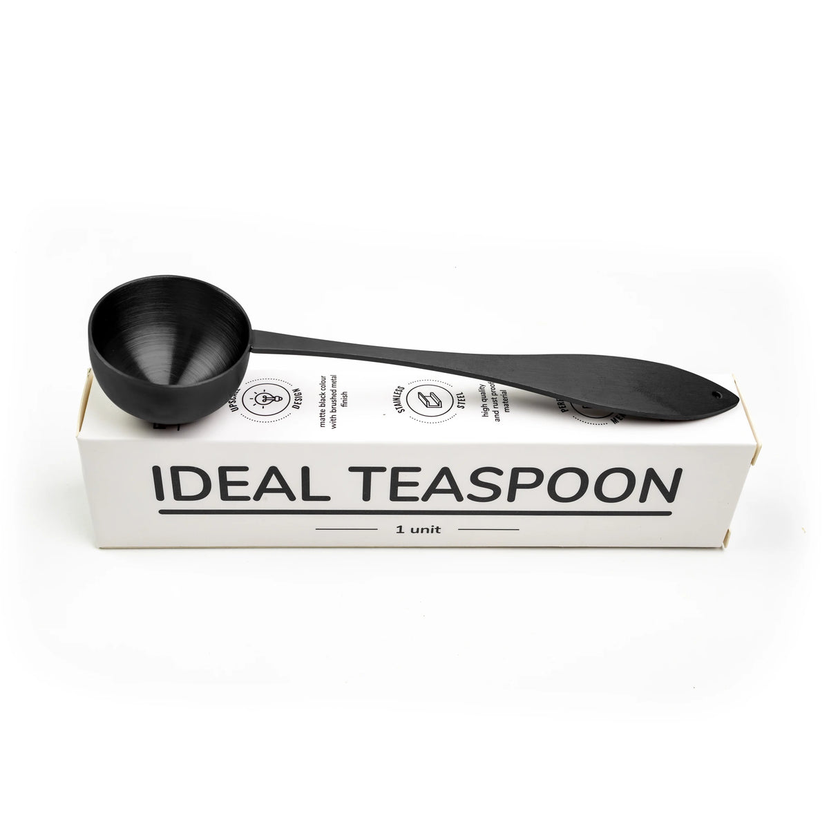Ideal tea spoon, matte black, resting on its box, on a white background