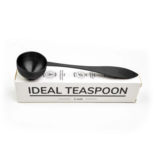 Ideal tea spoon, matte black, resting on its box, on a white background