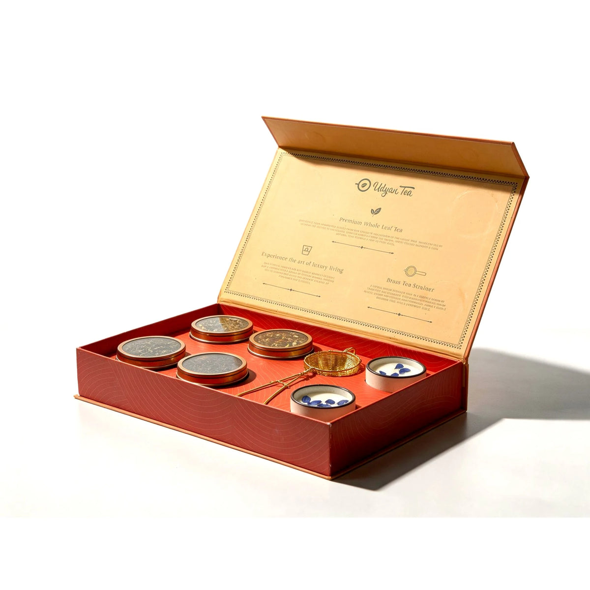 Meraki gift box open on a white background, with four teas, a brass strainer and two candles